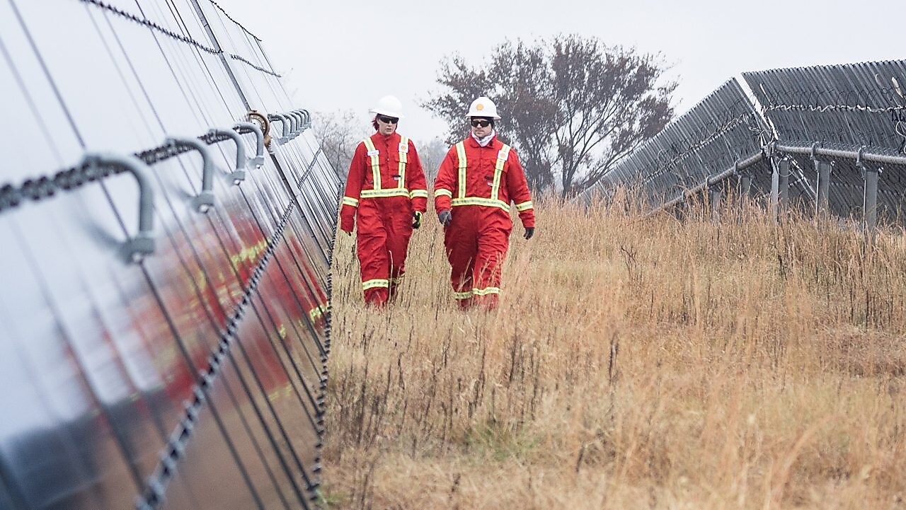 Two Shell employees walking between massive solar panels