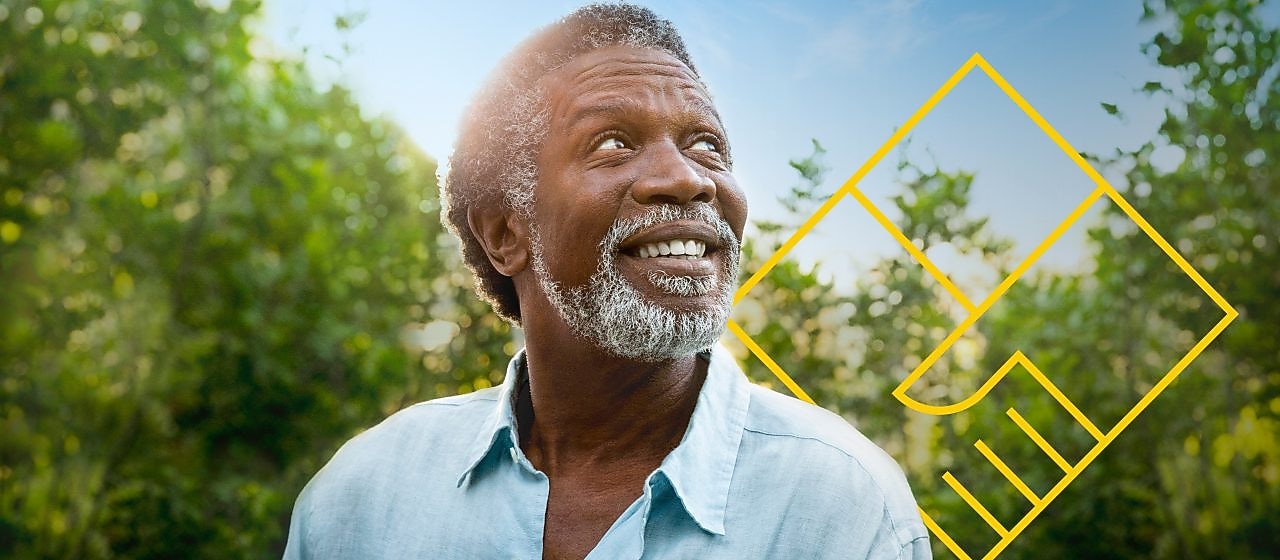 Бородатий чоловік посміхається на тлі дерев і графічного зображення «Створення цінності для акціонерів»