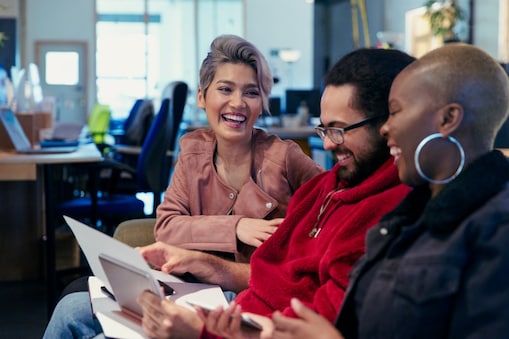 Троє людей в офісі сидять поруч, дивляться на папери й сміються