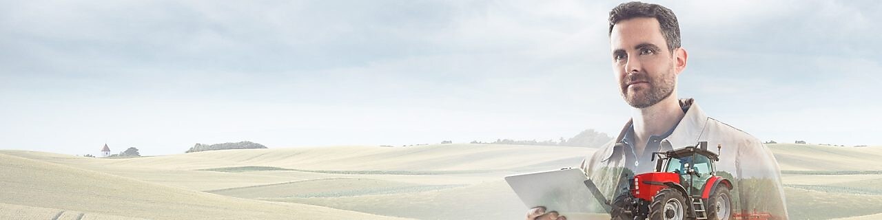 чоловік читає документ на тлі поля і червоного трактора