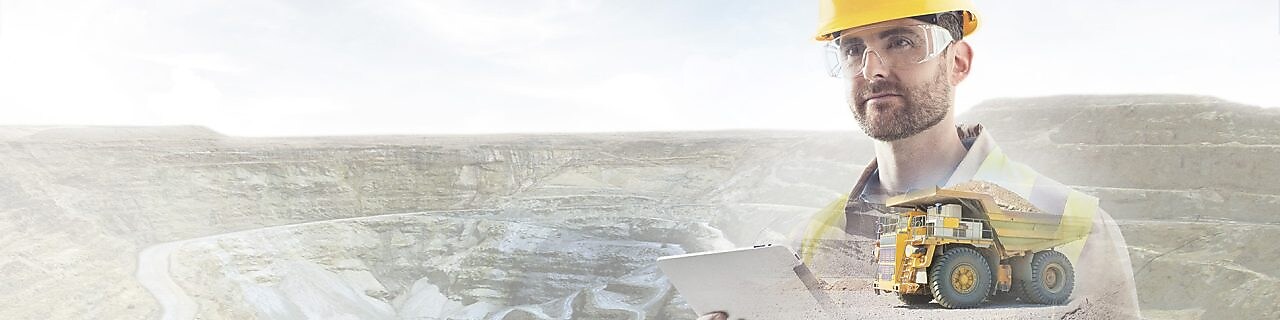 робітник в жовтій касці на тлі кручі і великої жовтої вантажівки