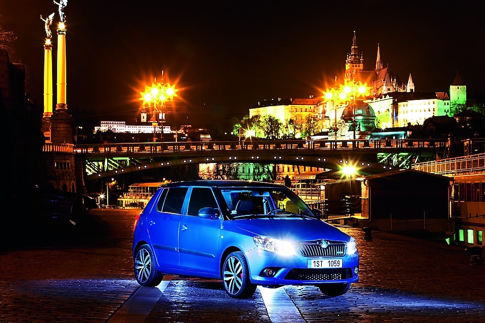 Синій автомобіль вночі стоїть на Празькій дорозі. На тлі зображений міст і замок