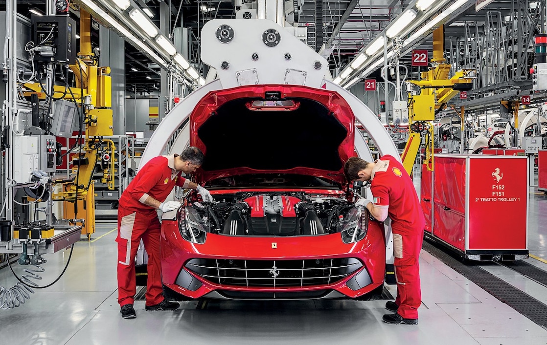 Червоний Ferrari стоїть на заправному терміналі станції «Шелл», чоловік спирається ліктем на заправну колонку